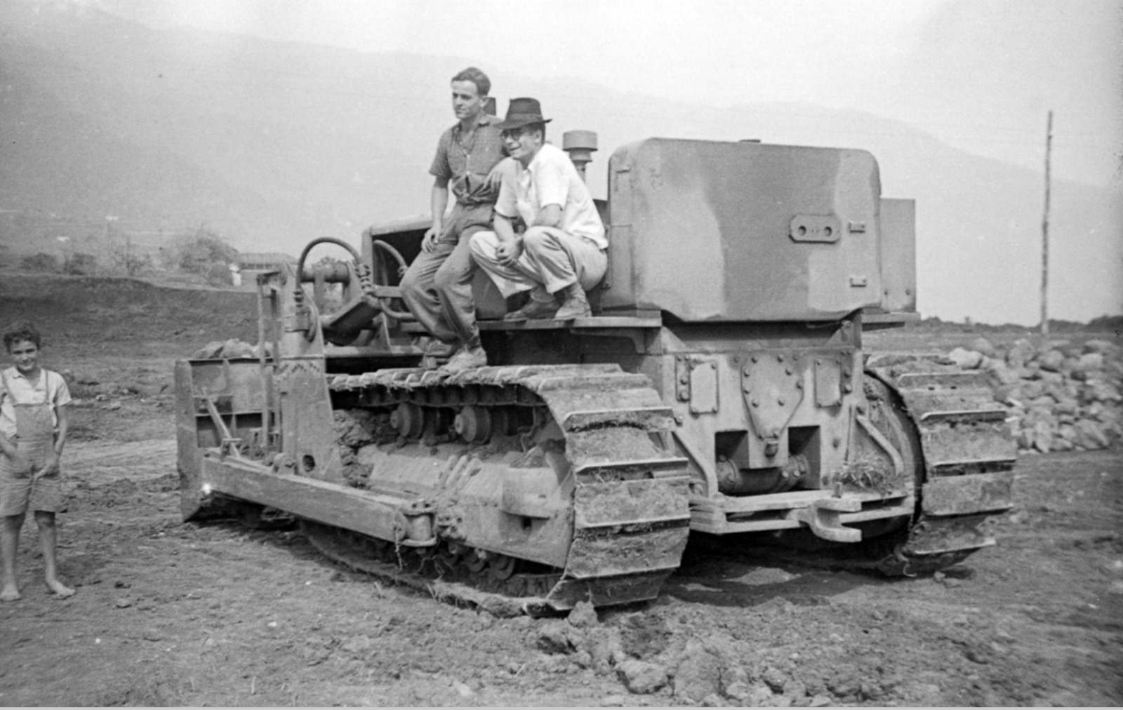 Pausa en el trabajo: dos hombres descansan sobre el bulldozer mientras un niño descalzo, vecino del barrio, observa la escena.