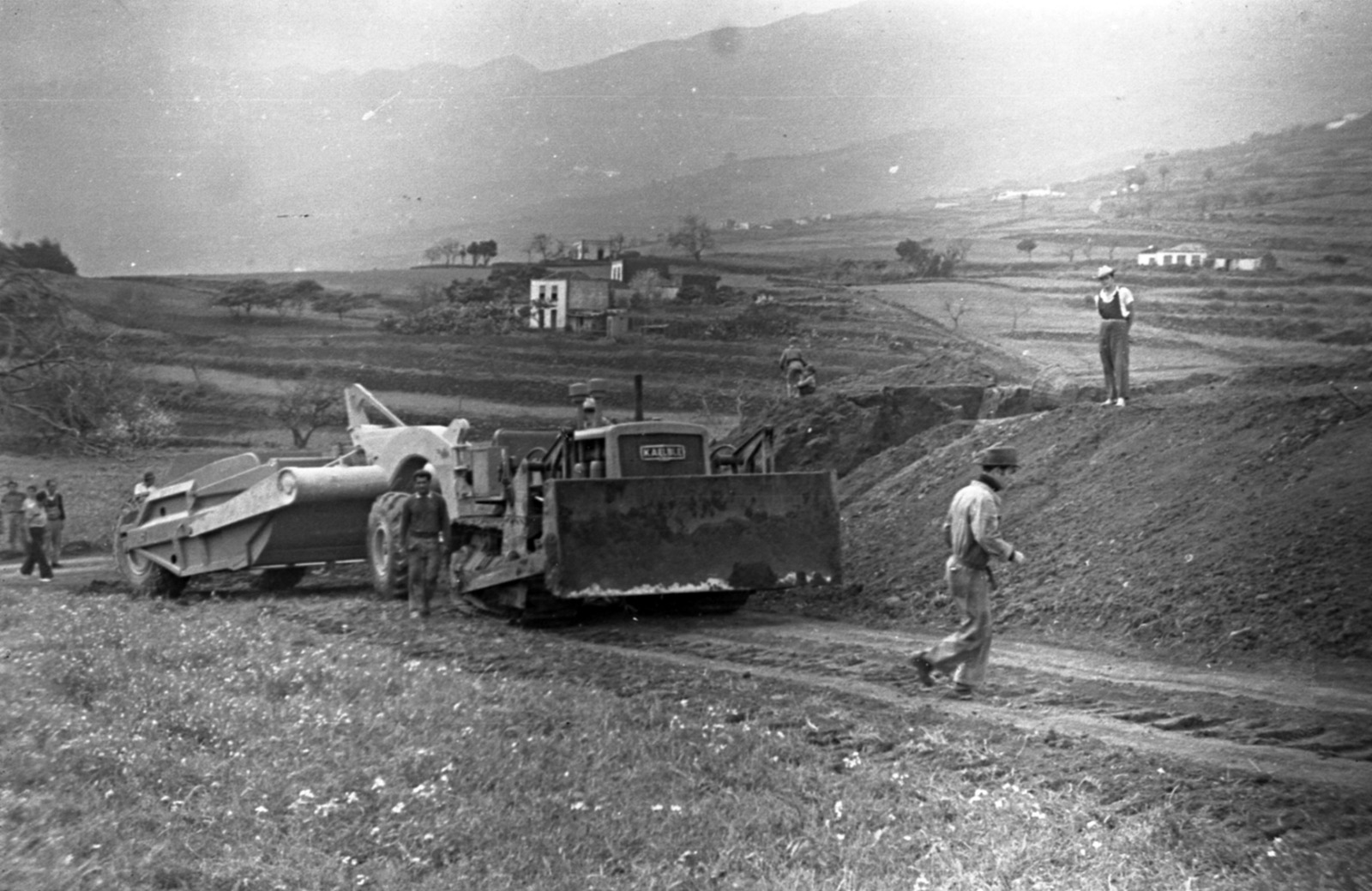 Un bulldozer Kaelble nivela la futura pista. Detrás, las terrazas de cultivo y las casas dispersas de Breña Alta.