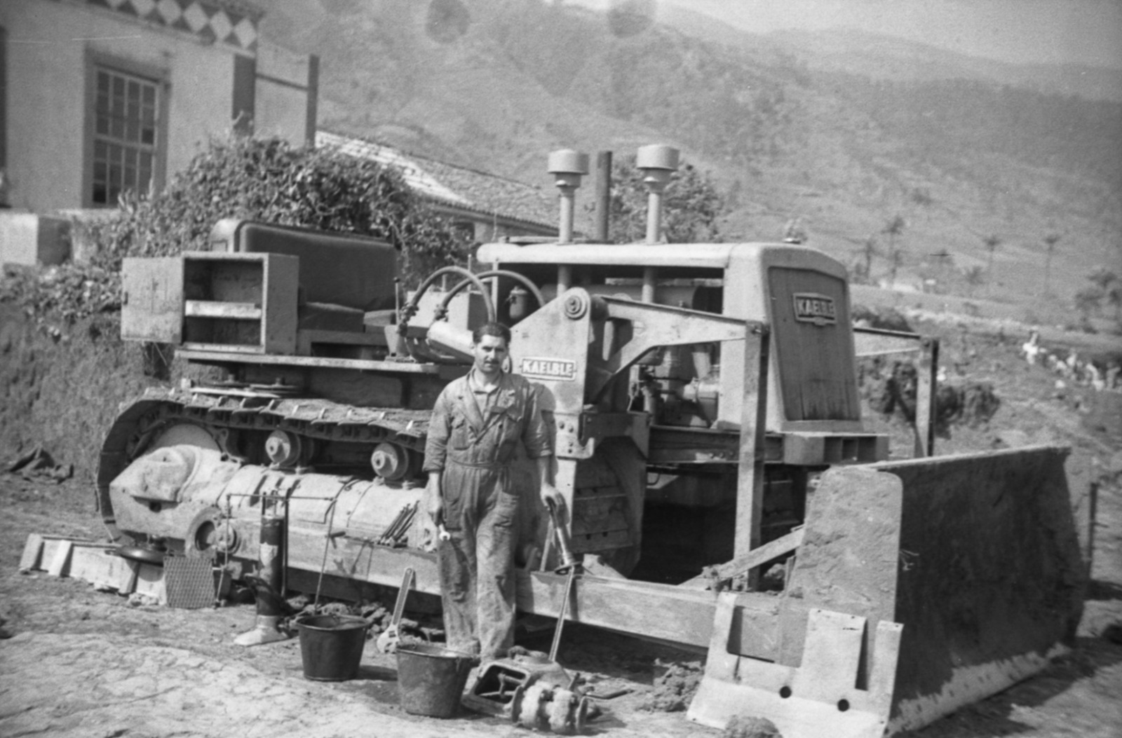 Retrato del bulldozer Kaelble con su operario junto a una casa palmera.