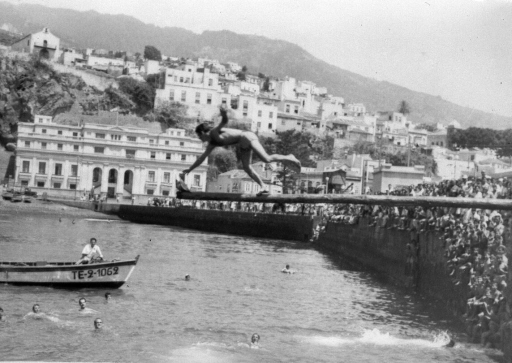 Un joven se lanza al agua desde el muro del malecón con la ciudad al fondo