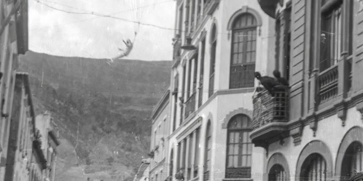 Paracaídas abriéndose en el aire entre las fachadas de la Calle Real
